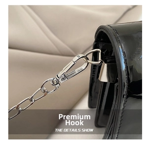 Detail of silver chain with lobster clasp on black patent leather shoulder bag