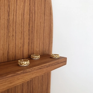 Macro detail of three-piece golden chain ring set with zircon and crown accents on wood