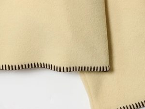 Close-up of beige wool fabric texture with black decorative whipstitch trim detail