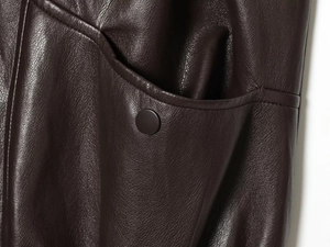 Detail of dark brown leather vest featuring a metallic snap button pocket and fine texture
