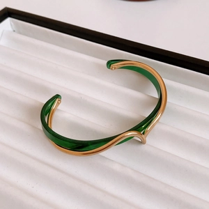 Detail of wave-shaped gold-plated bangle featuring layered translucent green inlay