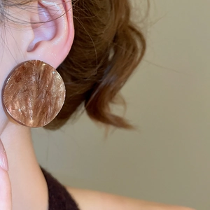 Close-up of oversized amber acrylic earrings with marbled texture on model