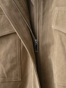 Close-up of brown suede jacket with silver metal zipper and stitched flap pocket detail