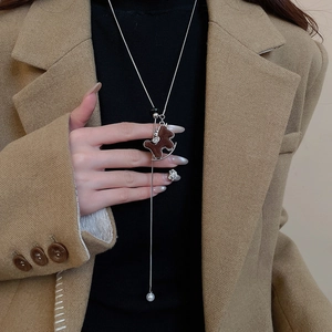 Detail of a silver-toned necklace featuring a brown flocked horse pendant and a white pearl drop