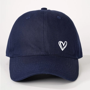 Detailed view of white heart embroidery on navy cotton canvas baseball cap surface