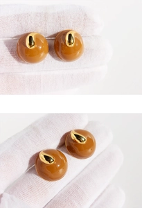 Macro shot of caramel brown enamel stud earring with gold metal accent on white glove