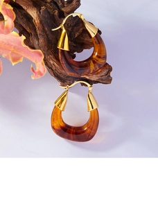 Detailed view of U-shaped earrings with amber resin and gold metal on a wooden branch