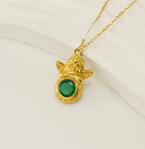 Gros plan du pendentif ange en or 18 carats tenant une pierre verte sur socle blanc