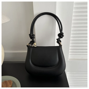 Detail of a chic black puffer saddle bag featuring a knotted shoulder strap and gold zipper