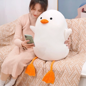 Giant white plush duck doll with long orange legs held by a person on a home sofa
