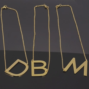 Détail de trois colliers en acier inoxydable 18K avec pendentifs lettres D, B et M
