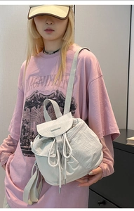 Adjustable straps on a white drawstring nylon bucket backpack shown on model back