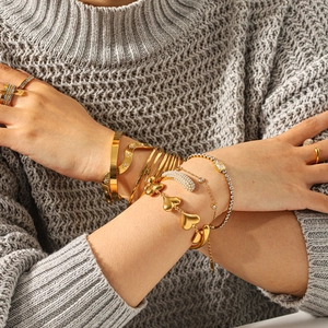Close-up of golden stainless steel heart bracelets and rings worn with layered jewelry style