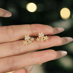 Golden S925 silver flower stud earrings with sparkling zircons shown on finger