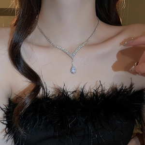 Close-up of V-shaped silver necklace with pear-shaped rhinestone on model with black feathers