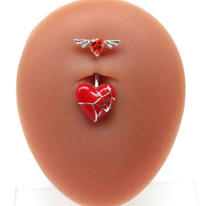 Detailed shot of a winged red heart belly button ring on a silicone skin model