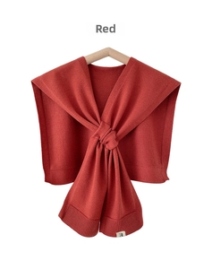 Detail of red knitted shawl accessory with ribbed texture and woven brand label on hanger