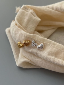 Close-up of gold and silver heart stud earrings with radial texture on linen bag
