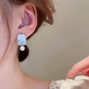 Detail shot of square silver earrings with blue texture and pearl drop on female model