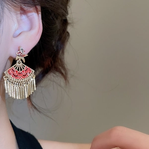 Close-up of golden fan-shaped fringe earrings with red enamel and crystals on a model