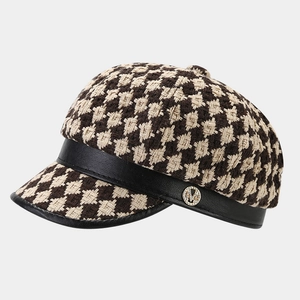 Detail of checkered newsboy hat with black leather brim and M-letter metal buckle