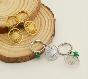 Detailed view of sunburst earrings in gold and silver with green bead accents on wood