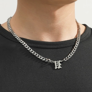 Close-up of silver Gothic letter H pendant on a Cuban link chain necklace worn by a model