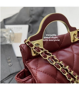 Detail of wine red quilted handbag with golden metal handle and woven chain strap