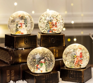 Close-up of lighted Christmas snow globes with Santa and snowman on vintage book base