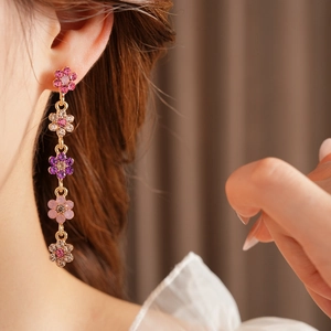 Detail of long floral tassel earrings with pink and purple crystals on golden metal