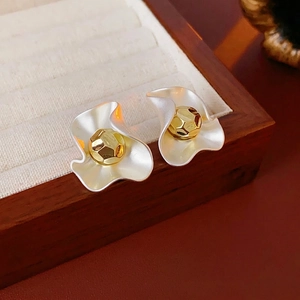 Asymmetric silver wave stud earrings with faceted gold center spheres on jewelry tray