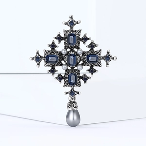 Baroque cross brooch with deep blue gems and grey pearls on a white minimalist background