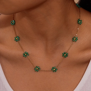 Detailed view of women floral necklace with emerald green beads on a gold chain