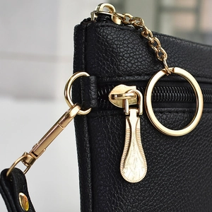 Close-up of black lychee grain leather with gold zipper and chain on small crossbody bag