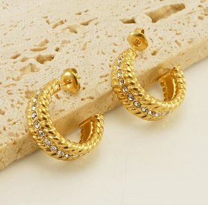 Macro detail of gold U-shaped twisted hoop earrings with crystals on stone base