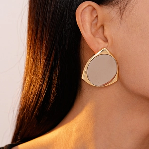 Detail of a large gold geometric triangle mirror earring on model with warm lighting