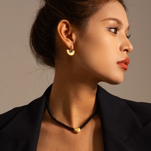 Close-up of black beaded necklace with textured gold heart pendant on a model