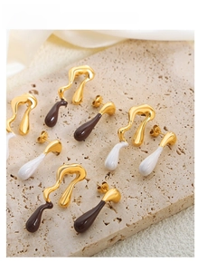 Detail of asymmetric gold earrings with brown and white drip glaze on stone