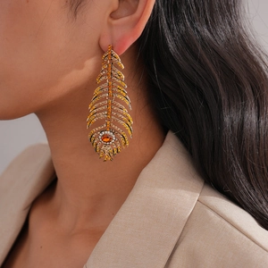 Gros plan de boucles d'oreilles plumes dorées avec strass jaunes et orange sur modèle