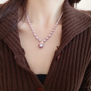 Gros plan d'un collier de perles mauves avec pendentif doré porté sur un tricot
