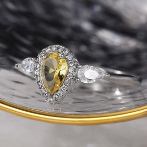 Macro shot of yellow pear-shaped zircon ring with halo setting on a glass surface