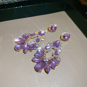 Close-up of golden tassel earrings with purple teardrop crystals and sparkling rhinestones