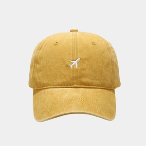 Detail of a ginger yellow washed cotton baseball cap featuring a white airplane embroidery
