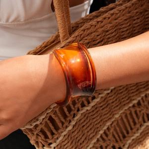 Macro view of wide amber resin bangle with irregular wave design worn by model