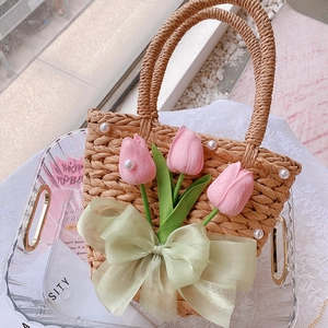 Detail of straw woven crossbody bag featuring pink tulips, pearls, and a green ribbon bow