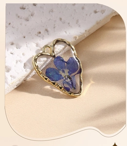 Detail of heart-shaped gold earring featuring a real blue dried daisy in resin