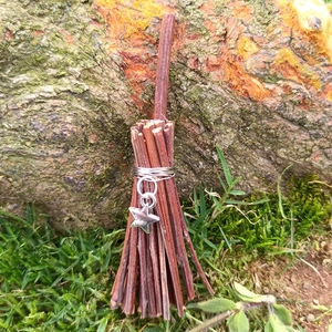 Miniature handmade witch broom pendant with silver star charm in an outdoor setting