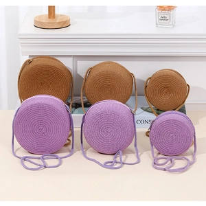 Close-up of round straw woven crossbody bags in khaki and lavender with three sizes