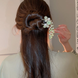 Detail einer eleganten chinesischen Haarnadel mit grünen Perlen und Quasten im Haar