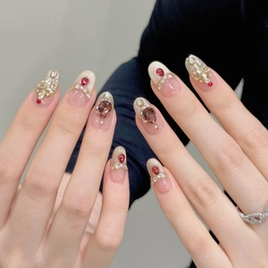 Detalle de uñas hechas a mano con gemas rojas, estrellas doradas y perlas sobre base